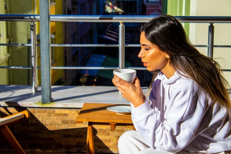 Mulher relaxando com uma xícara de café à luz do sol, representando uma rotina leve e prazerosa inspirada em dias de férias.