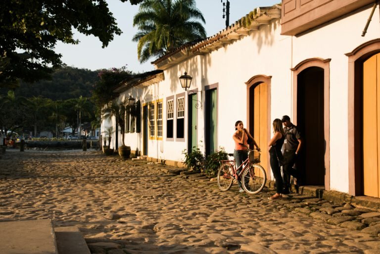 Rua de vila litorânea com casas coloridas, moradores caminhando sob a luz do fim da tarde, representando o estilo de vida à beira-mar no litoral brasileiro.